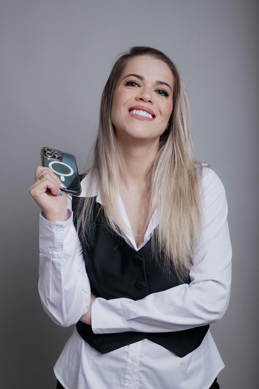 Thienne Giardino sorrindo, com colete preto e camisa branca, segurando o celular