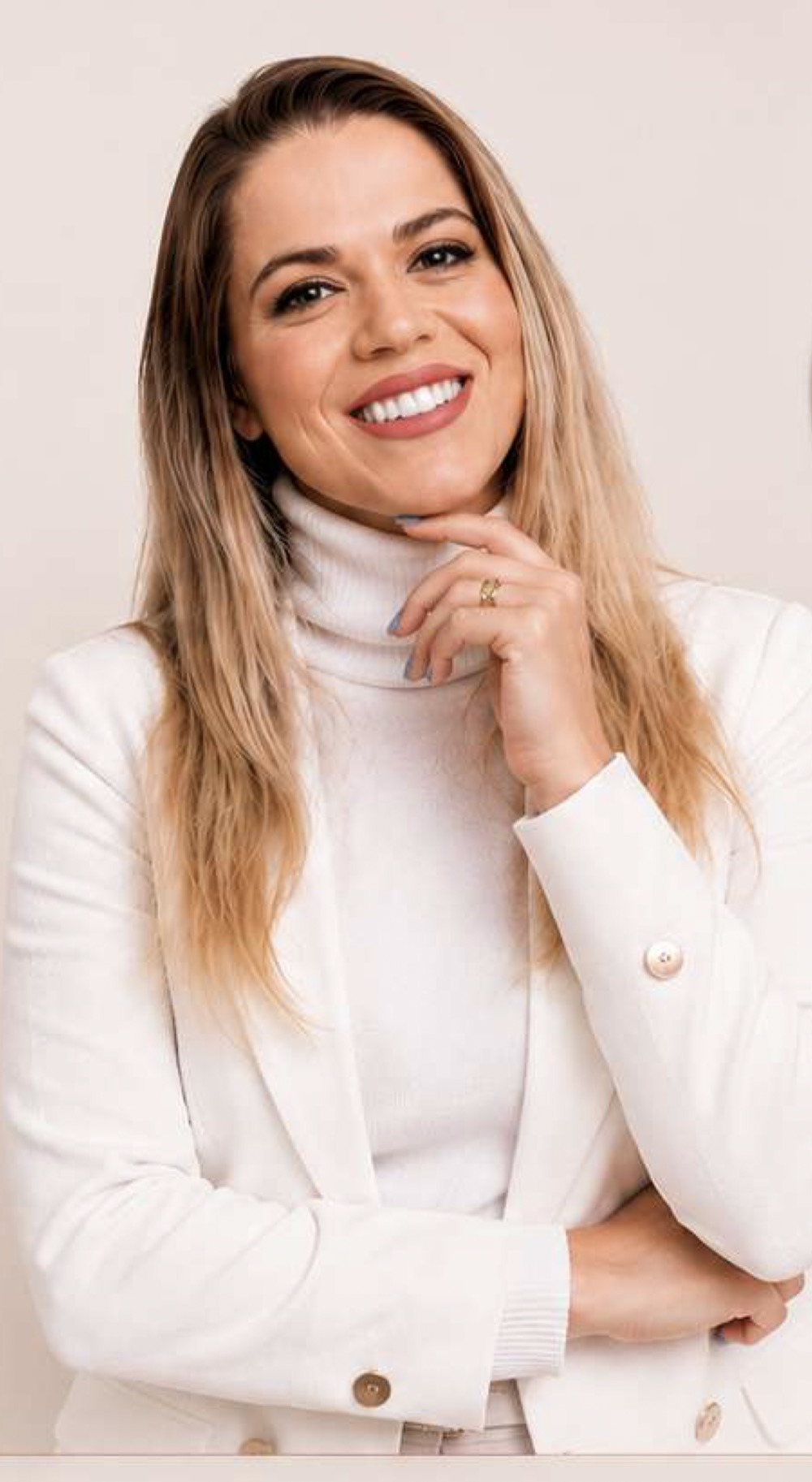 Retrato de Thienne Giardino sorrindo, com blazer branco e mão apoiada no queixo